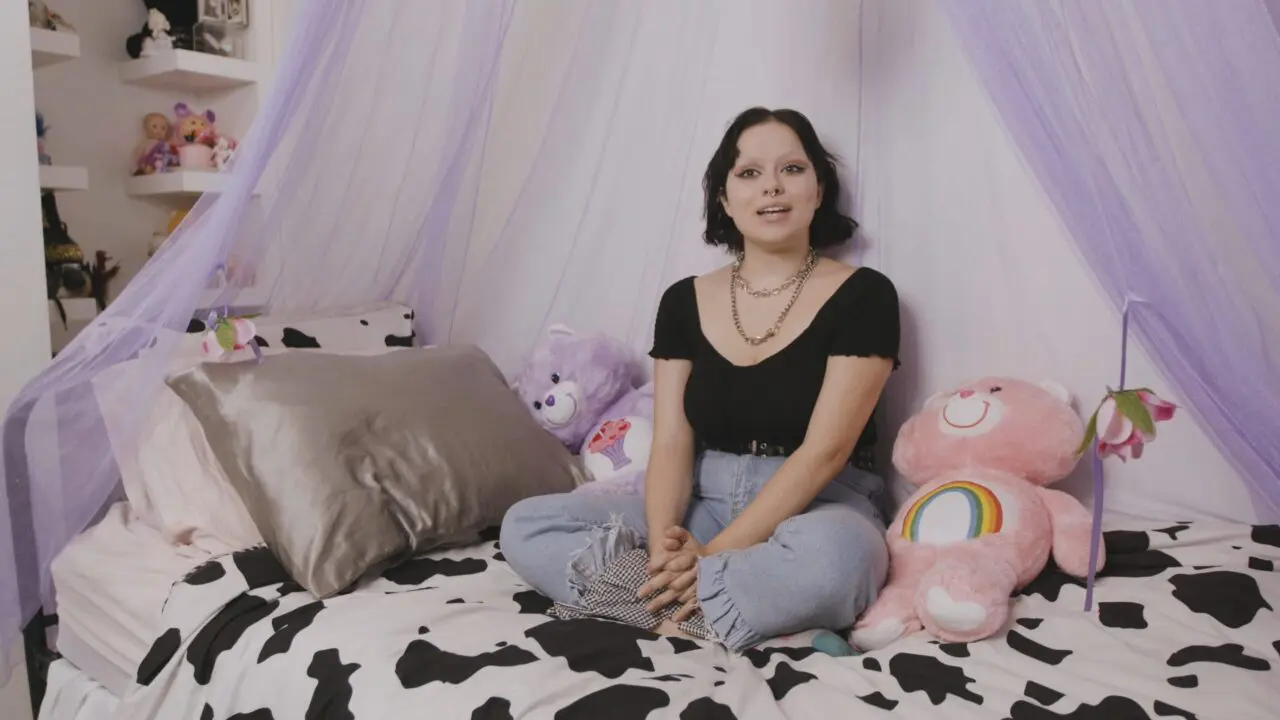 Person sitting on bed with teddy bears, wearing casual outfit, surrounded by soft toys.