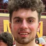 Smiling person with short curly hair in a casual indoor sports setting.