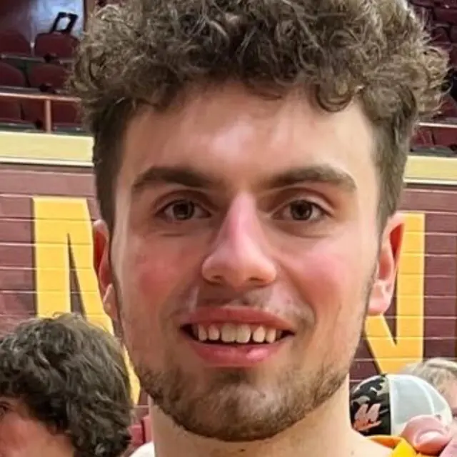 Smiling person with short curly hair in a casual indoor sports setting.