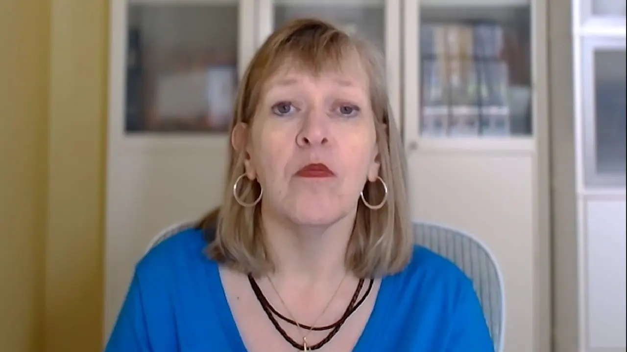 Smiling woman in a blue shirt with short hair and hoop earrings.