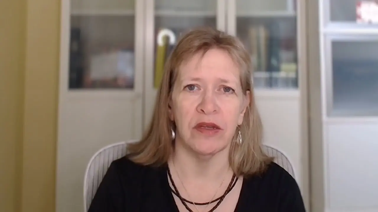 A person speaking on a video call in an office setting.