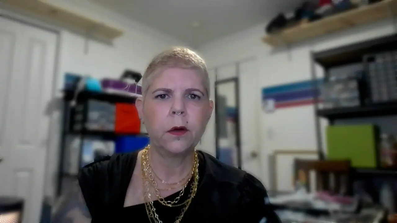 Person wearing gold chains in a cluttered workspace with focus on expression.